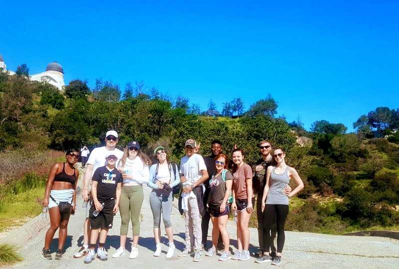 Diverse group of young people posing after a hike with Griffith Observatory in background.