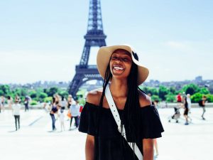 young lady wearing dark clothes and light hat smiles