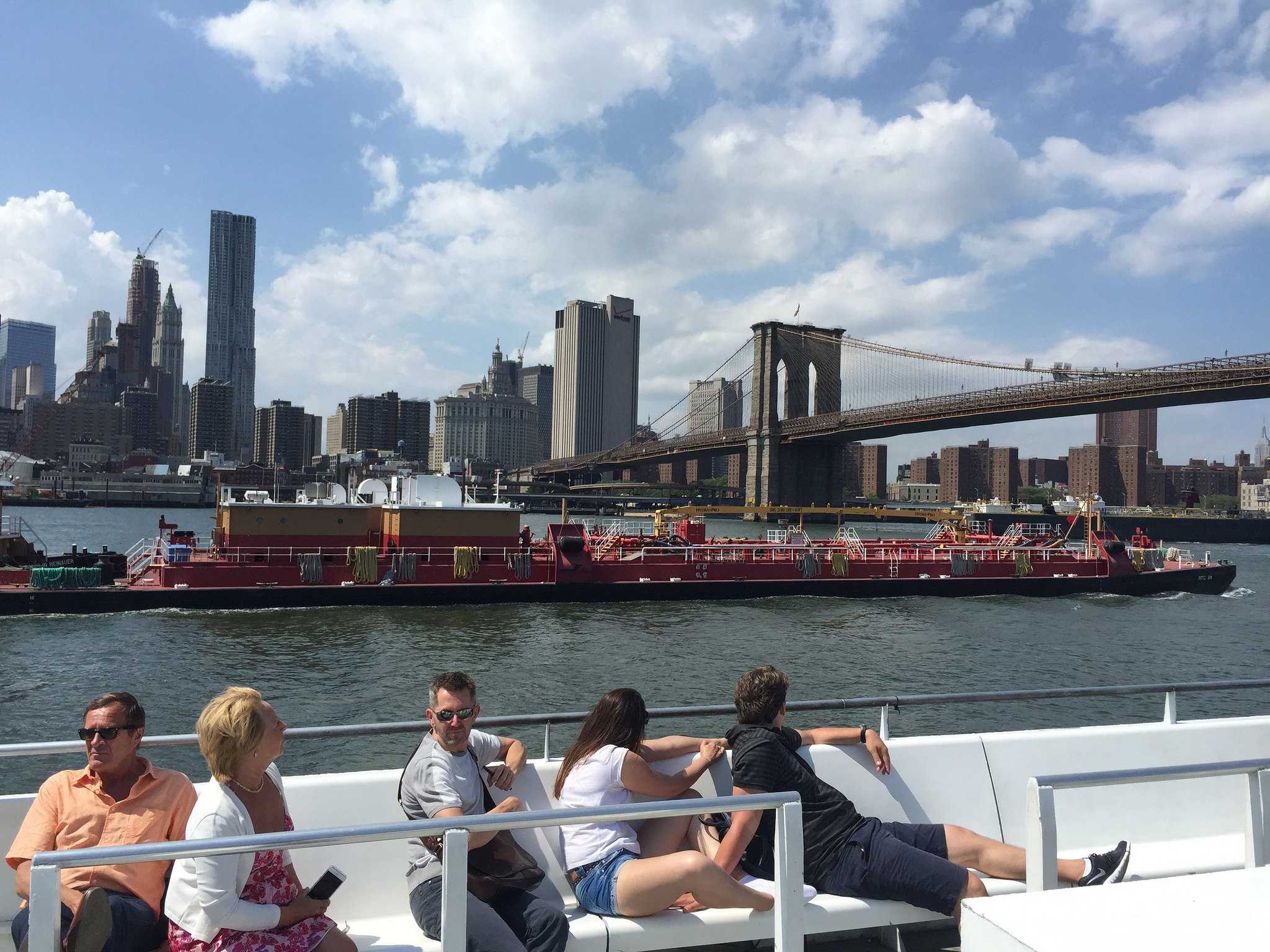 People riding on a boat past the brooklyn bridge