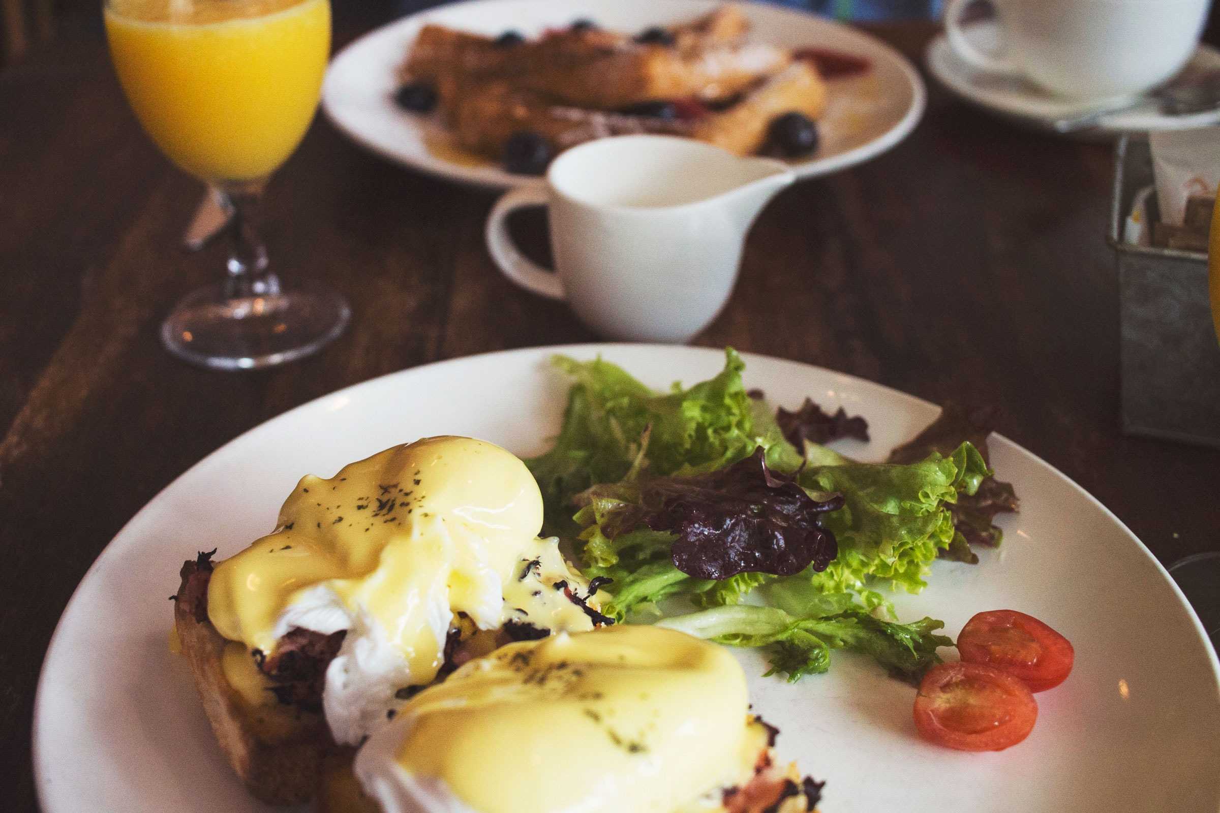 Plate of eggs benedict and side salad with glass of orange juice