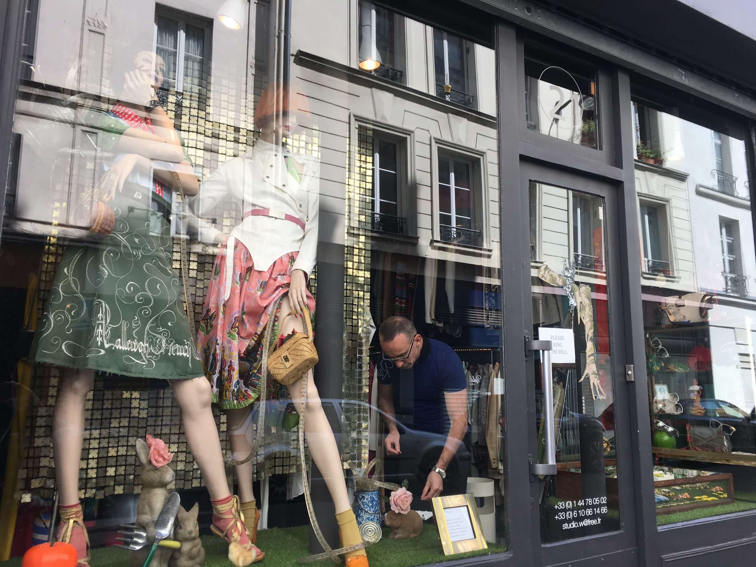 Man fixng a display with two mannequins dressed in vintage dresses in a shop window