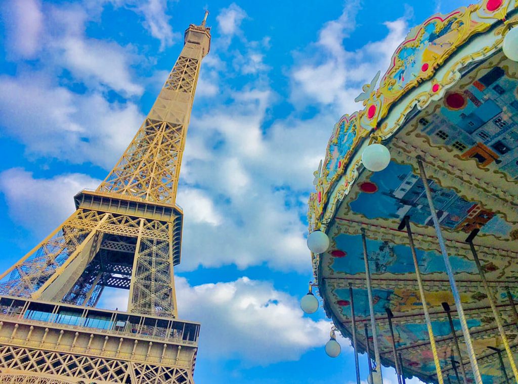 The Eiffel Tower and a portion of a carousel with a vibrant blue sky with fluffly white clouds