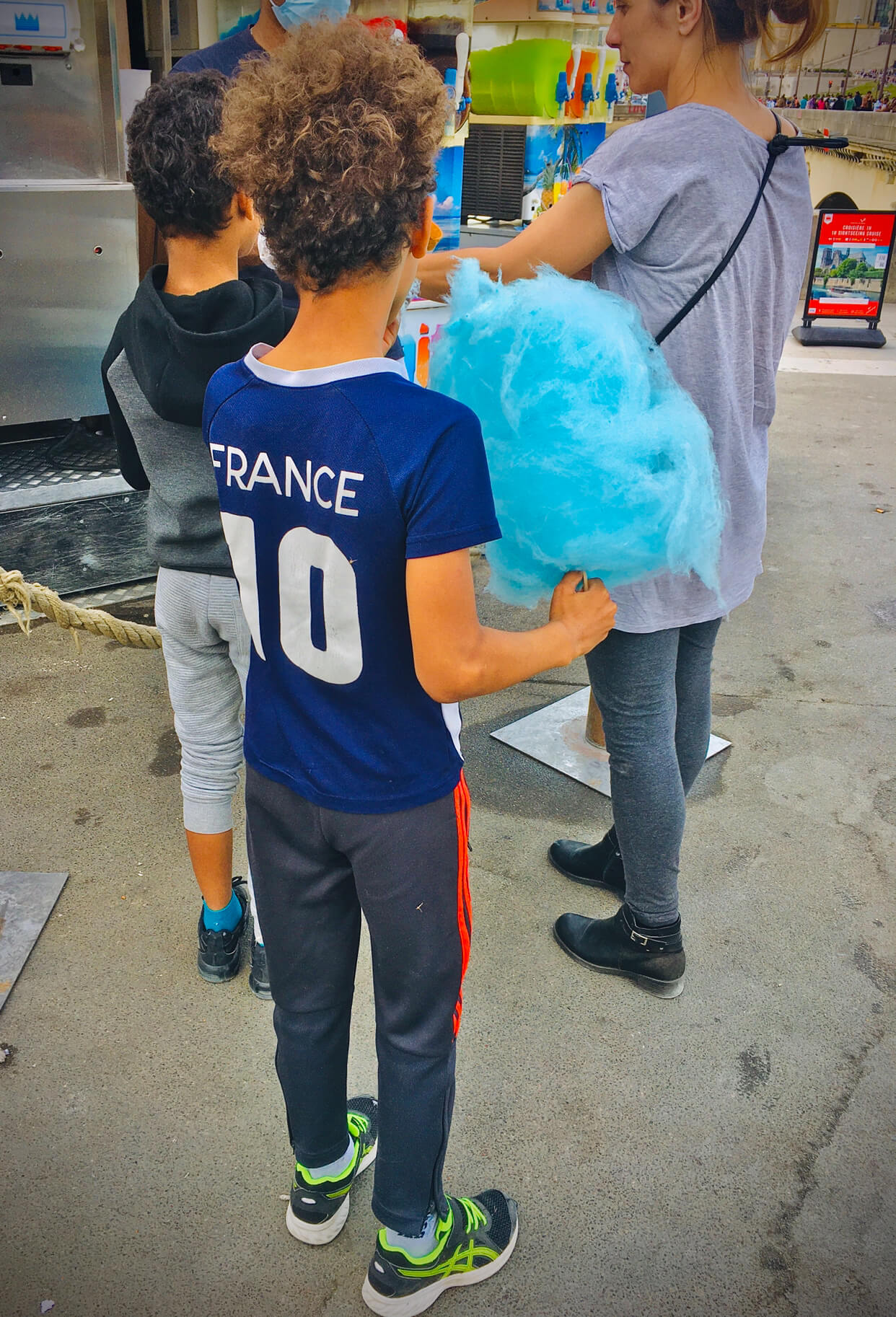 A boy with a jersey that says France 10 eats a big, blue puff of cotton candy