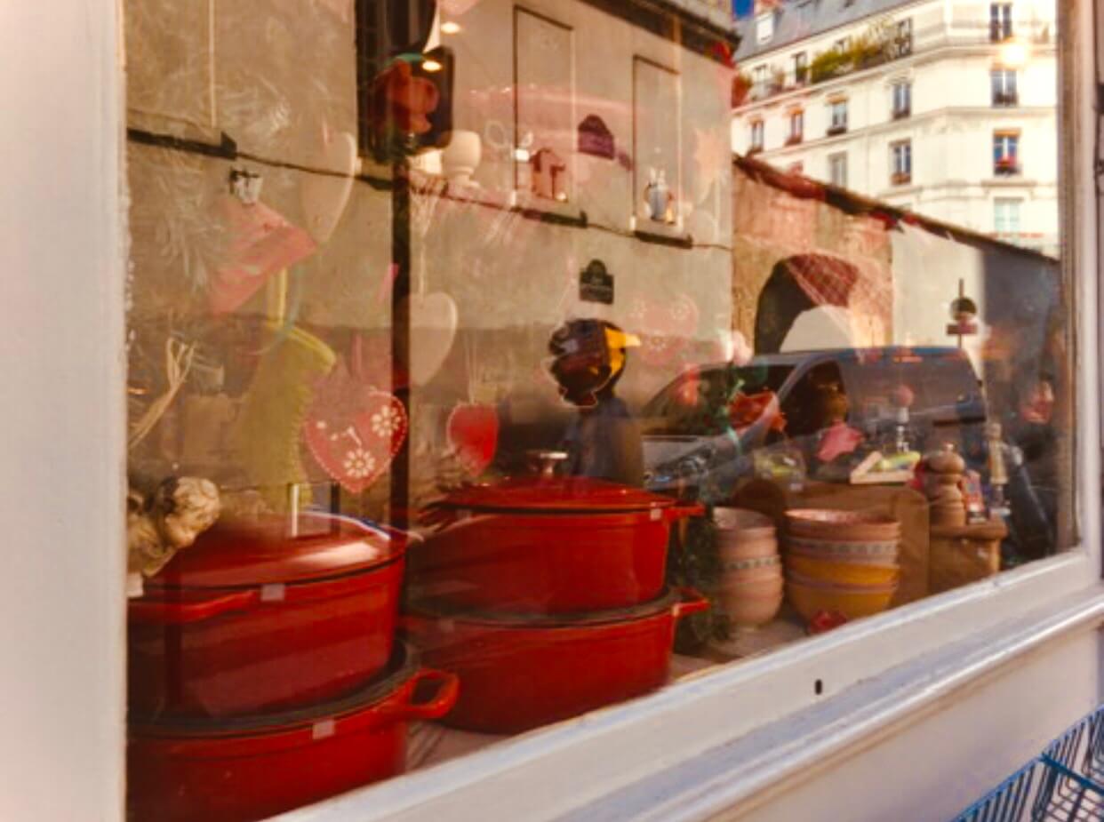 Red dutch oven cookware and bowls and ornaments on display in a window