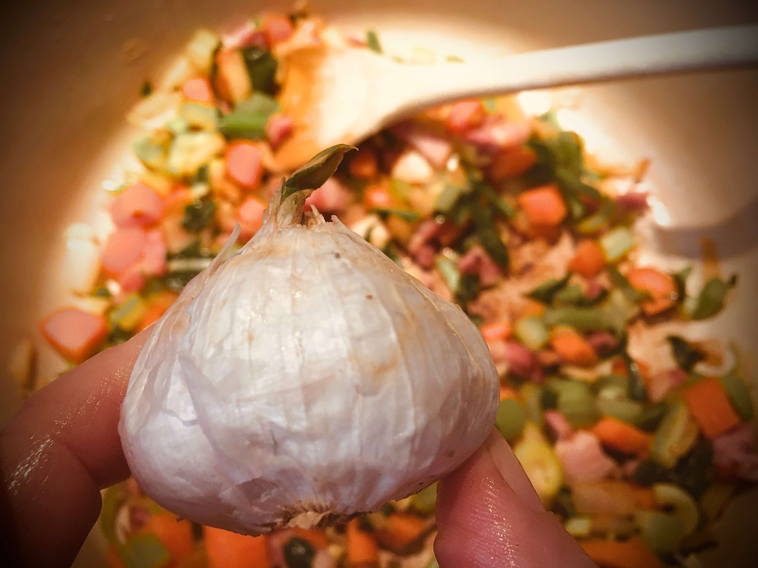 A small head of garlic over a pan of sautéed vegetables 