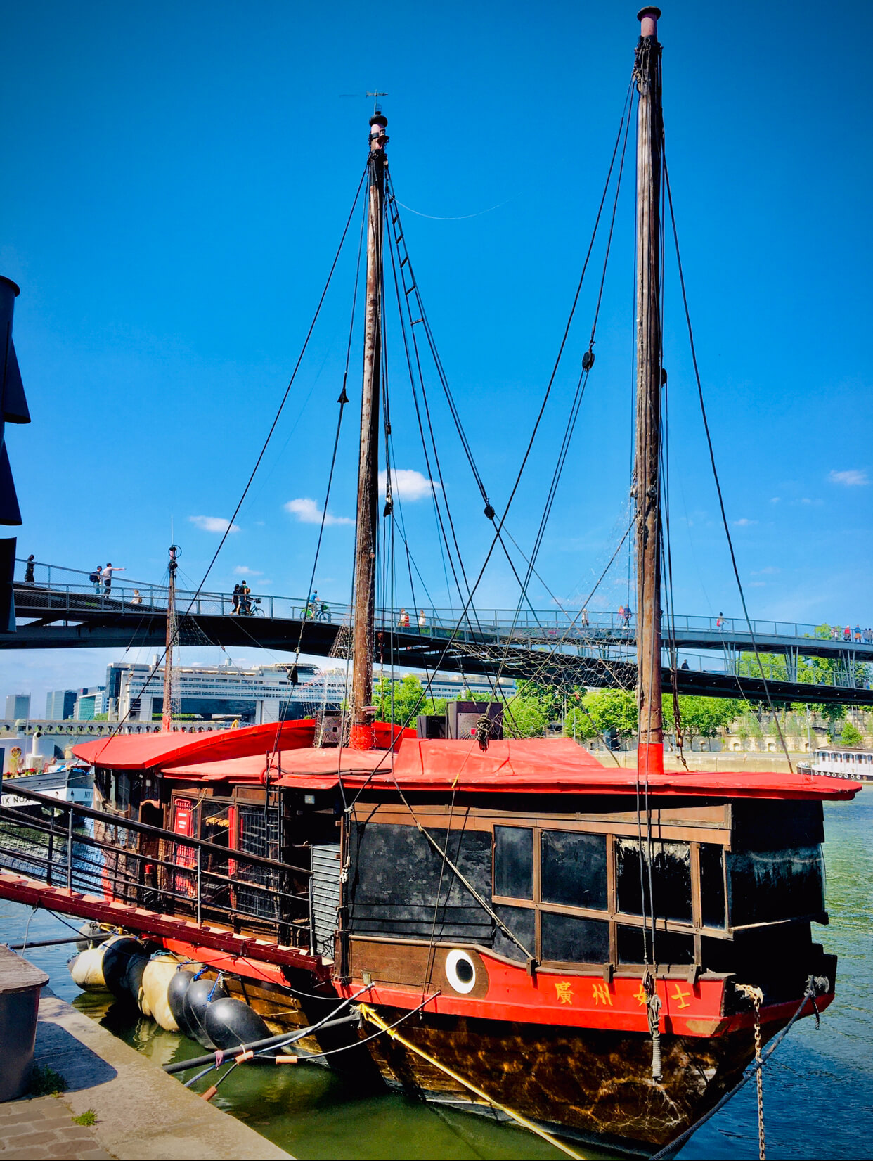 Red Chinese-style junkboat floating on the Seine river with blue sky and a bridge behind it