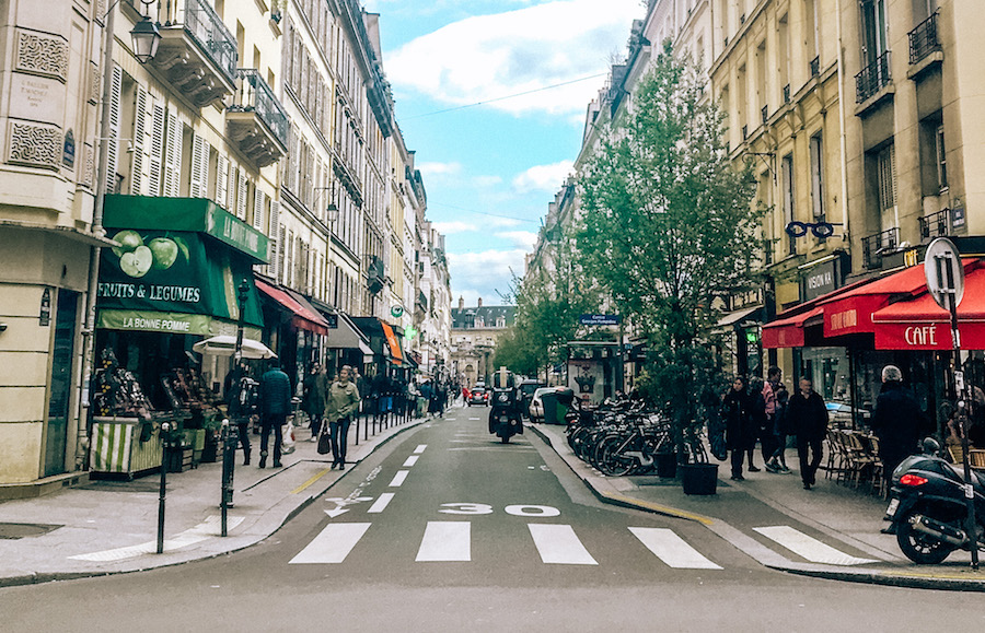 A scene from the streets of Paris with pedestrians, scooters, and shops