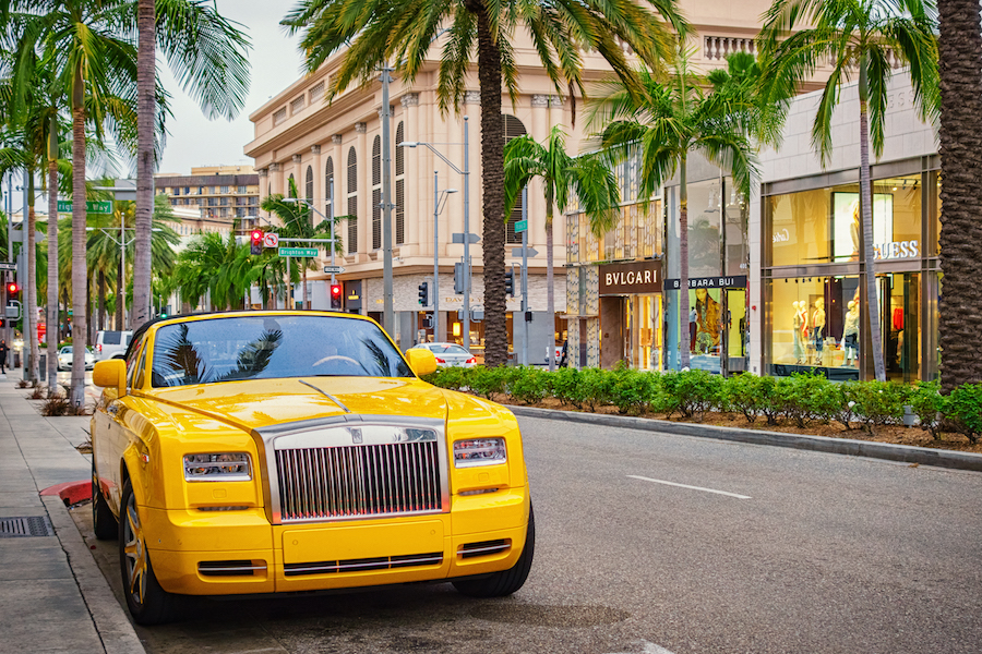 A yellow colored Rolls-Royce Phantom convertible parked on Rodeo Drive with luxury stores in the background in Beverly Hills, Los Angeles, California