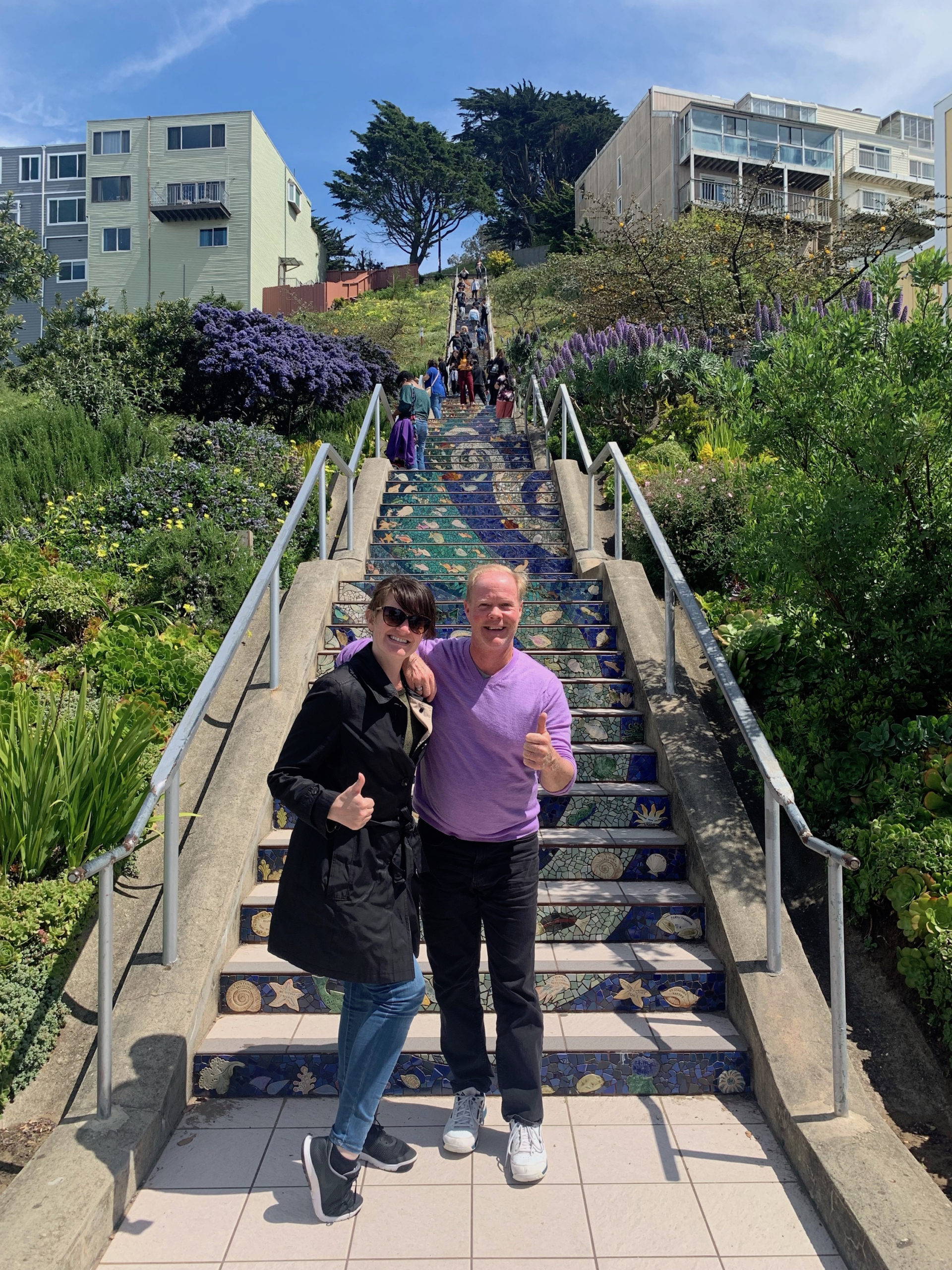 Two people posing for a photo in front of the 16th Avenue Tiled Steps