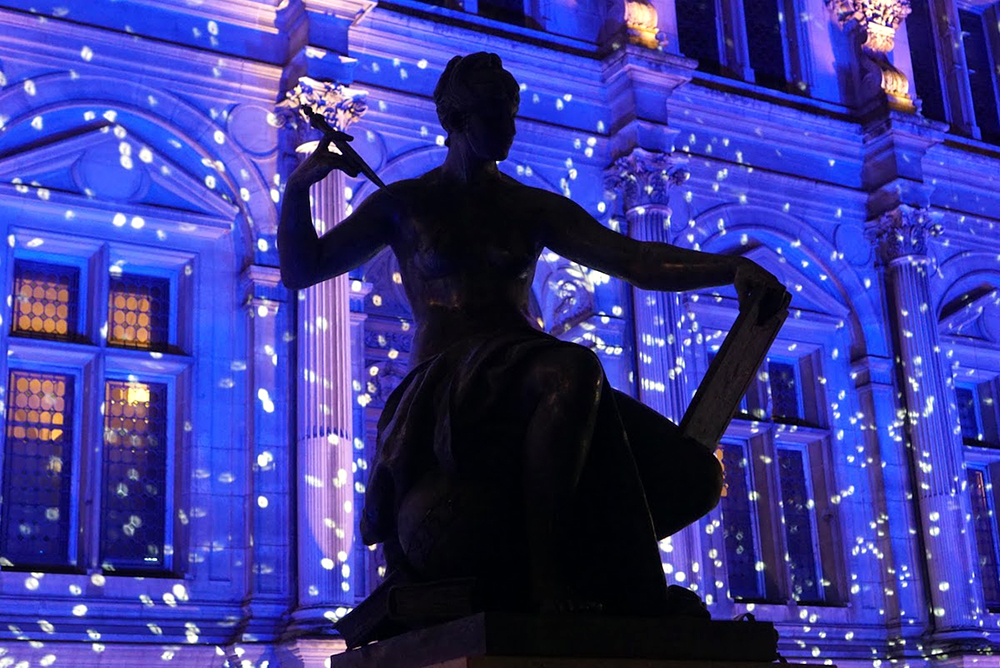 Statue in front the Hôtel de Ville in Paris lit with holiday lights