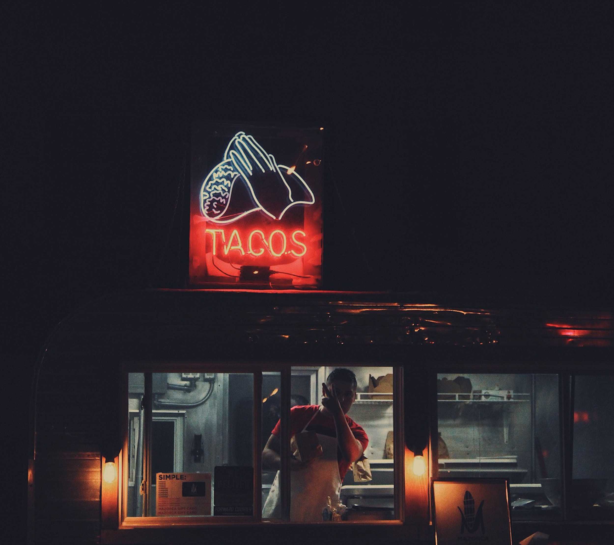 Lights that say taco and a man behind a window
