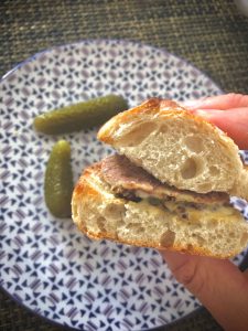 A small sandwich of pate on a baguette with two cornichons 