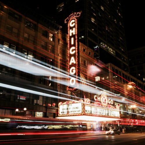 The iconic Chicago Theatre marquee glows with the word “CHICAGO” in bright lights against the city backdrop.