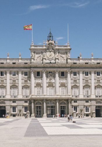 a large building with columns and a flag on top with Royal Palace of Madrid in the background