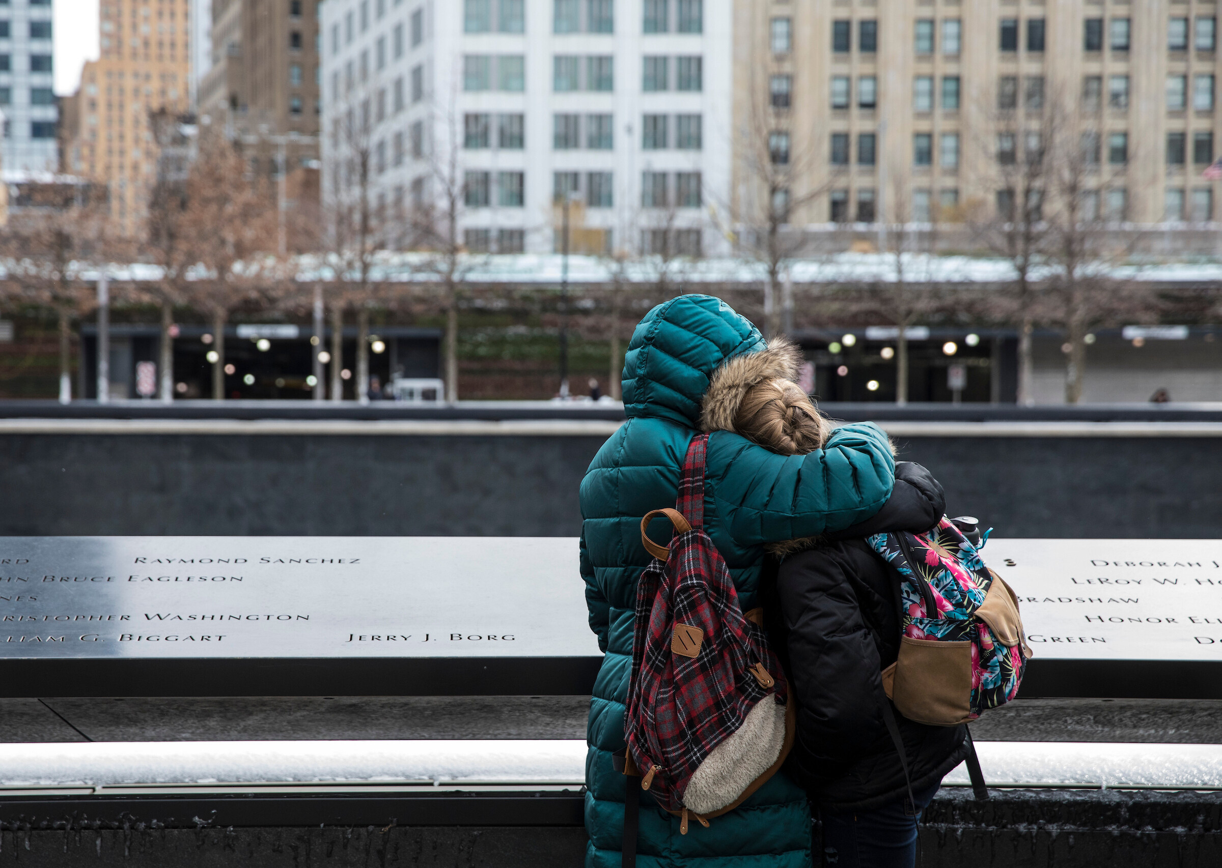 Two people comfort each other with a hug at the 911 Memorial in NYC