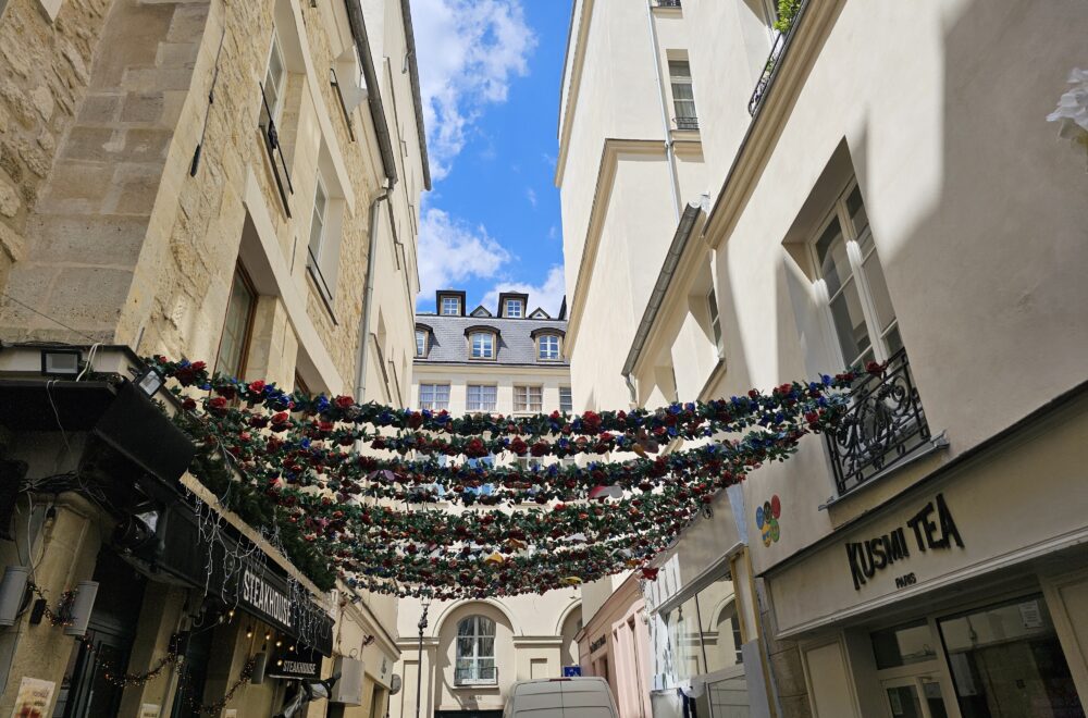 Decorative string lights and classic Parisian balconies over a narrow Le Marais street.