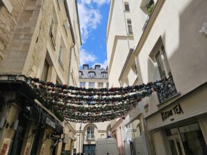 Decorative string lights and classic Parisian balconies over a narrow Le Marais street.