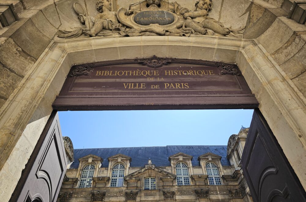 View of the Hôtel de Ville's ornate stone archway and rooftop in Paris’ Le Marais district.