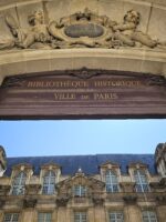 View of the Hôtel de Ville's ornate stone archway and rooftop in Paris’ Le Marais district.