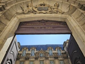 View of the Hôtel de Ville's ornate stone archway and rooftop in Paris’ Le Marais district.