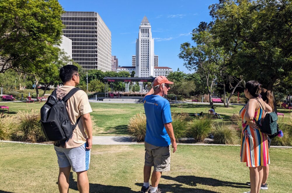 Small tour group standing in El Pueblo Historic Park with Los Angeles City Hall visible in the background.