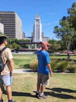 Small tour group standing in El Pueblo Historic Park with Los Angeles City Hall visible in the background.