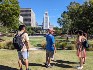 Small tour group standing in El Pueblo Historic Park with Los Angeles City Hall visible in the background.