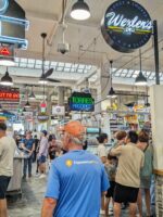 Visitors exploring food stalls at Grand Central Market in Los Angeles, with hanging neon signs and a lively crowd.