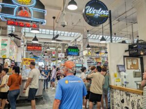 Visitors exploring food stalls at Grand Central Market in Los Angeles, with hanging neon signs and a lively crowd.