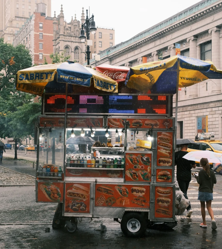 A food cart with umbrellas on a city street in NYC