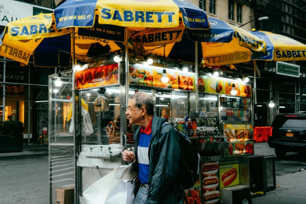 Elderly man walking past hot dog stand in NYC