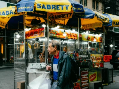 Elderly man walking past hot dog stand in NYC