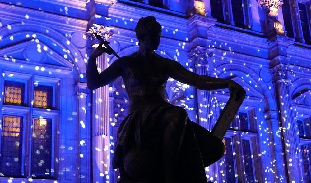 Statue in front the Hôtel de Ville in Paris lit with holiday lights